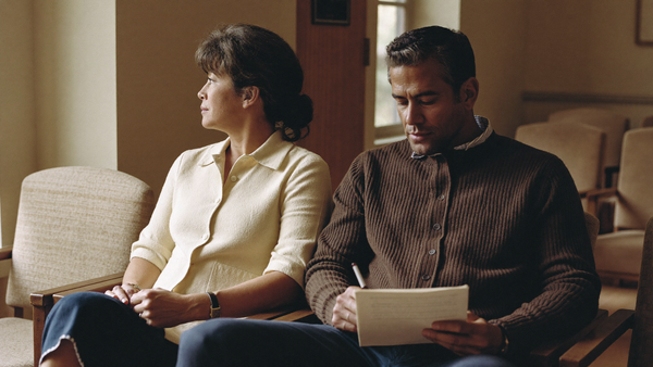 A woman and her husband sit together in a calm waiting area, reading a printed page before a perimenopause appointment.