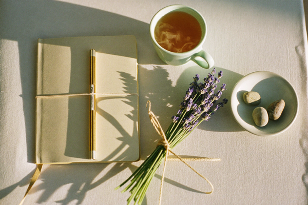 Flat lay of a cream notebook, dried lavender, and warm ceramics on cream linen