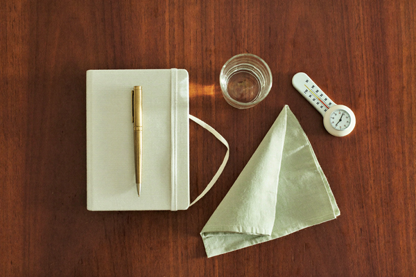 Overhead flat lay of a notebook, brass pen, and warm ceramics on walnut wood