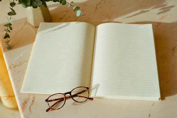 Blank ruled papers, tortoiseshell glasses, and eucalyptus on a marble surface in warm light