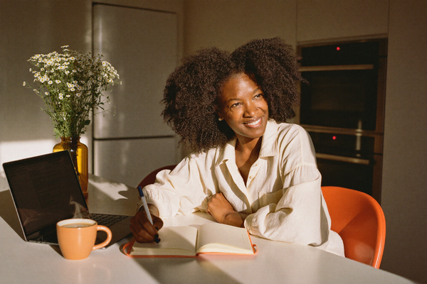 A confident woman at a kitchen table with laptop and notebook, warm afternoon light