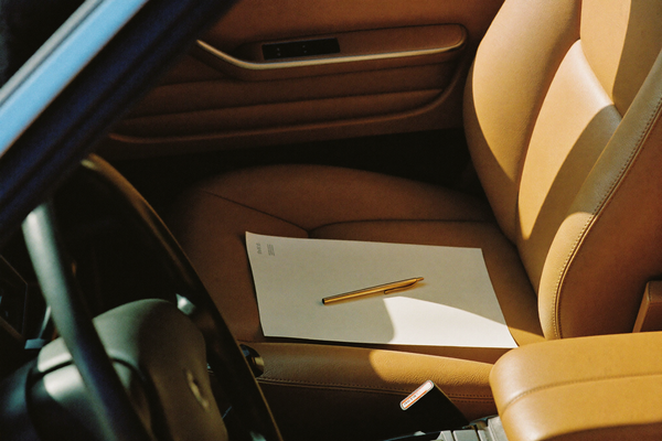 A blank cream paper and gold pen on a car passenger seat in warm afternoon sunlight