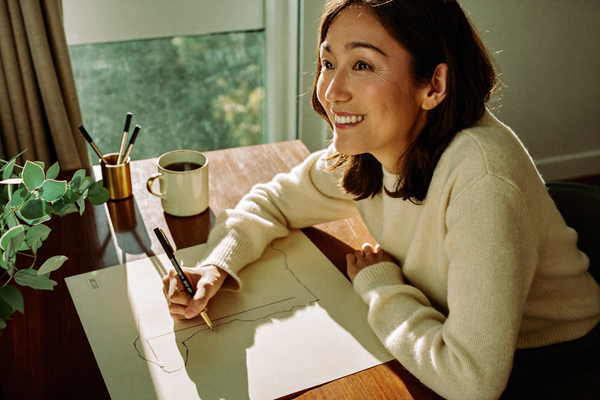 A woman at a warm walnut desk sketching a timeline on cream paper