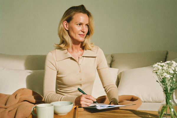 A confident woman sitting on a sunlit cream couch with cream leggings and cardigan