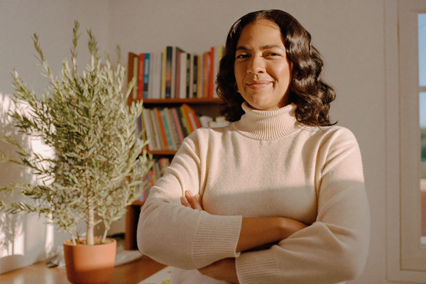 A confident woman in a warm home office beside a potted olive tree, morning light