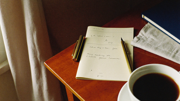 A cream printable page with a single handwritten sentence beside a brass pen and black coffee on a walnut desk