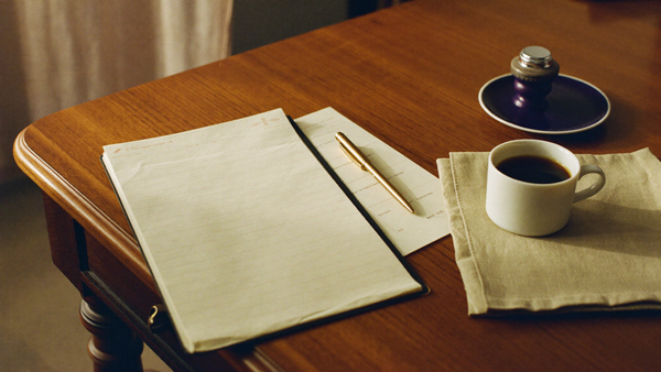 A cream printable bleeding log page with a brass pen and black coffee on a walnut desk, morning light